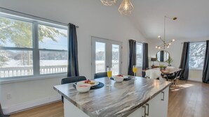 A modern kitchen with a marble countertop, a dining area with a table and chairs, and large windows with a view of a snowy landscape.