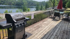 A wooden deck with a grill, outdoor furniture, and a view of a lake.