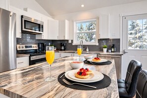 A modern kitchen with a marble countertop, stainless steel appliances, and a breakfast setting with waffles and fruit.