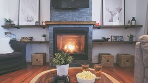 A cozy living room with a fireplace, wooden floors, a comfortable sofa, and a gaming setup.
