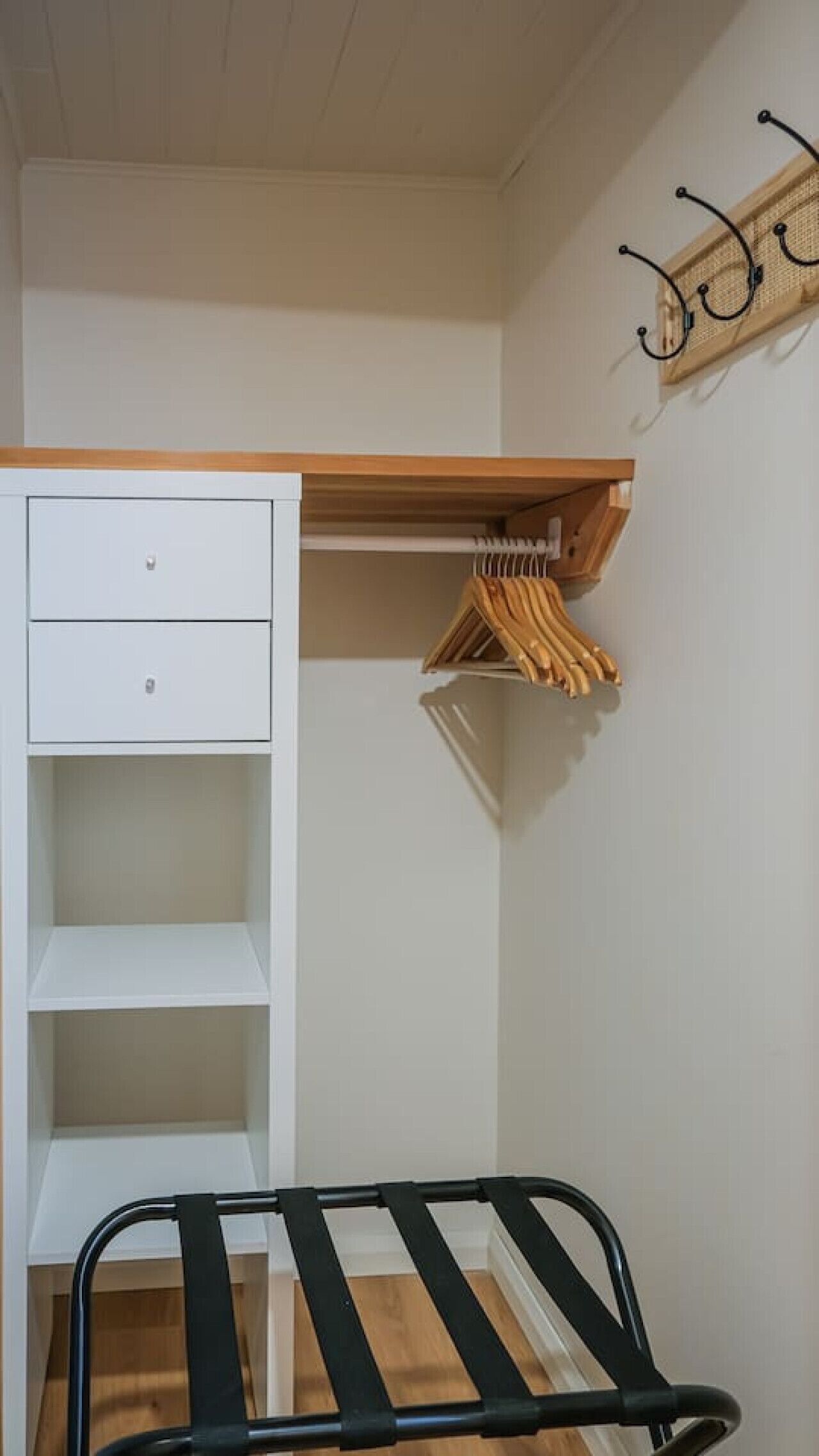 A bedroom with a bed, a white wardrobe, and a wooden shelf with hangers.