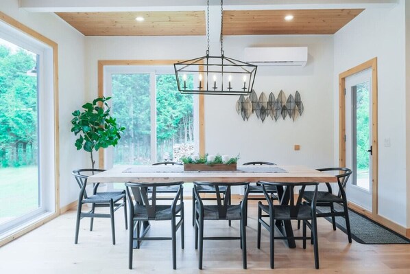 A dining area with a wooden table and chairs, a hanging light fixture, and a potted plant. - Tremblant Farmhouse w/Ski Hottub Fireplace Fondue Foosball Direct XC-Ski trails (La Conception)