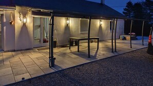 A covered outdoor area with a table and chairs, a bench, and a car parked nearby. - House with covered swimming pool and pétanque court (Lanchéres)