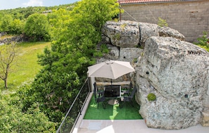 Un patio con mesa y sillas, un paraguas y vistas a un paisaje verde exuberante y una formación rocosa.