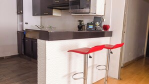 A kitchen with a white textured backsplash, a microwave, and a coffee machine on the counter. There are two red bar stools with metal legs. - New Cozy San Pedro Home Patio Work Area (San Pedro Garza García)