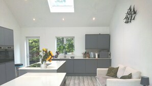 Una cocina moderna con una isla central, un comedor con mesa blanca y un espacio de estar con sofá y lámpara.