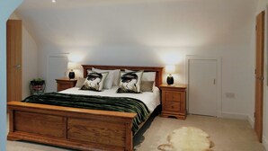 Un dormitorio con techo inclinado, una cama de madera con manta verde, dos lámparas de noche y una alfombra blanca y esponjosa.