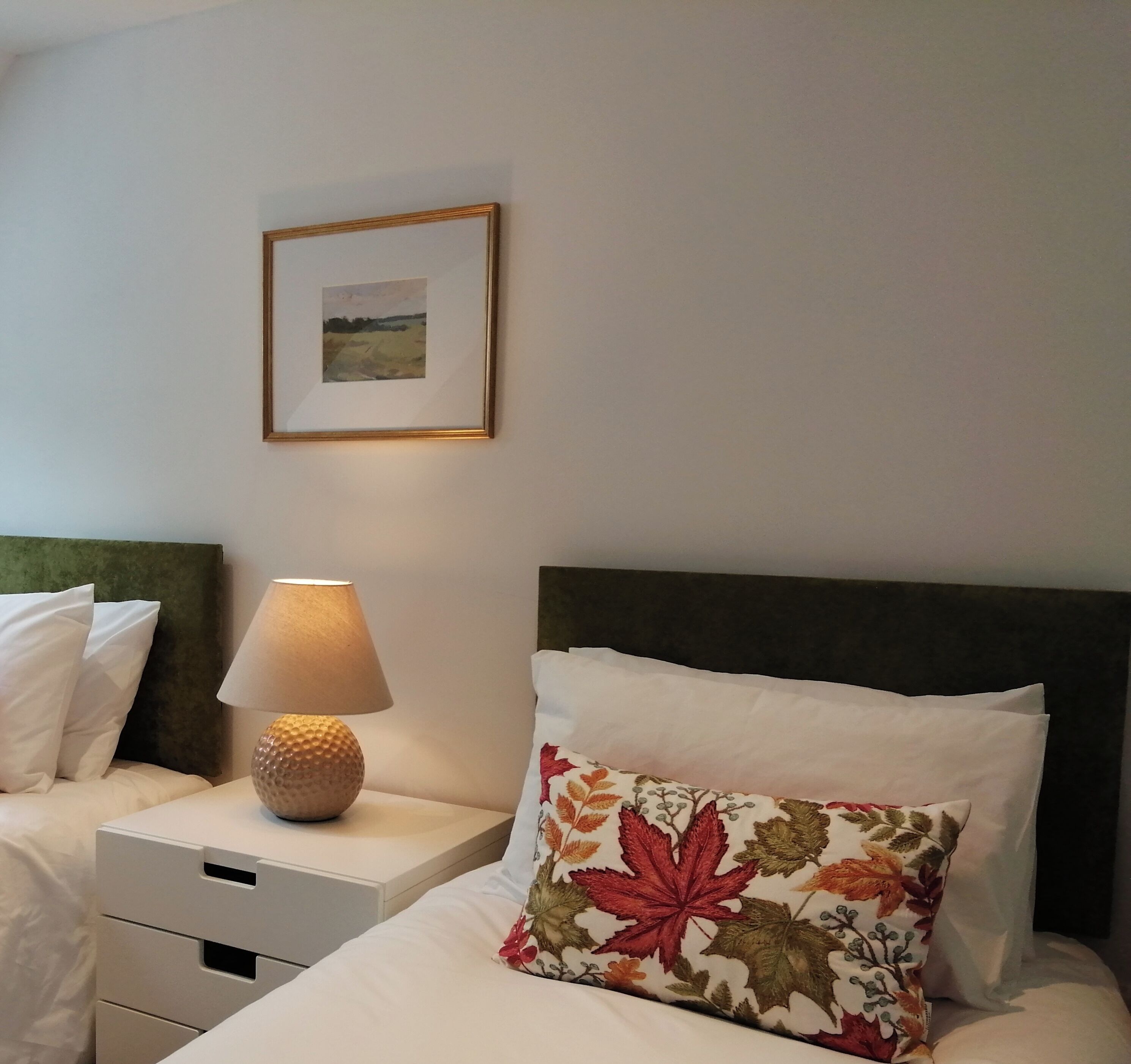 Ein Hotelzimmer mit Bett, Nachttisch mit Lampe, einem gerahmten Bild an der Wand und einem Zierkissen.