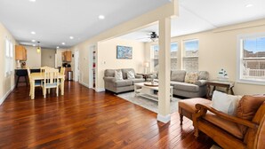 A spacious living area with hardwood flooring, a dining table, sofas, and a kitchen in the background. - Bay view-walk to beach/boards/restaurants, parking (Ventnor City)