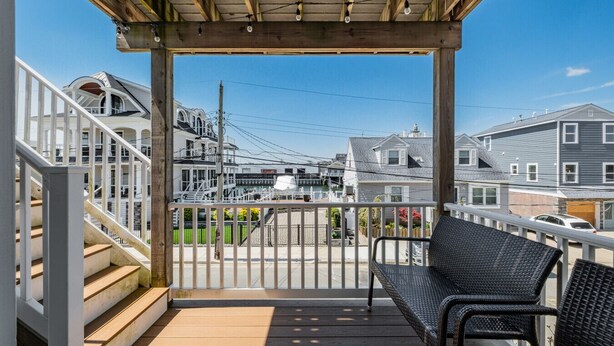 A covered outdoor area with a wooden deck, a metal railing, and a black wicker chair. - Bay view-walk to beach/boards/restaurants, parking (Ventnor City)
