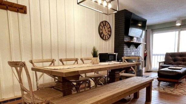 Une table à manger en bois avec des chaises, une horloge au mur et une cheminée.