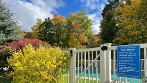 Un espace piscine clos, agrémenté d’un panneau indiquant les règles d’utilisation, entouré d’un feuillage automnal et surplombé d’un ciel dégagé.