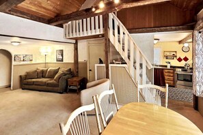 A cozy living room with a sofa, a dining table with chairs, a staircase, and a kitchen area. - Walk to Pickle Barrel & Jax. Hot tub & Views (Killington)