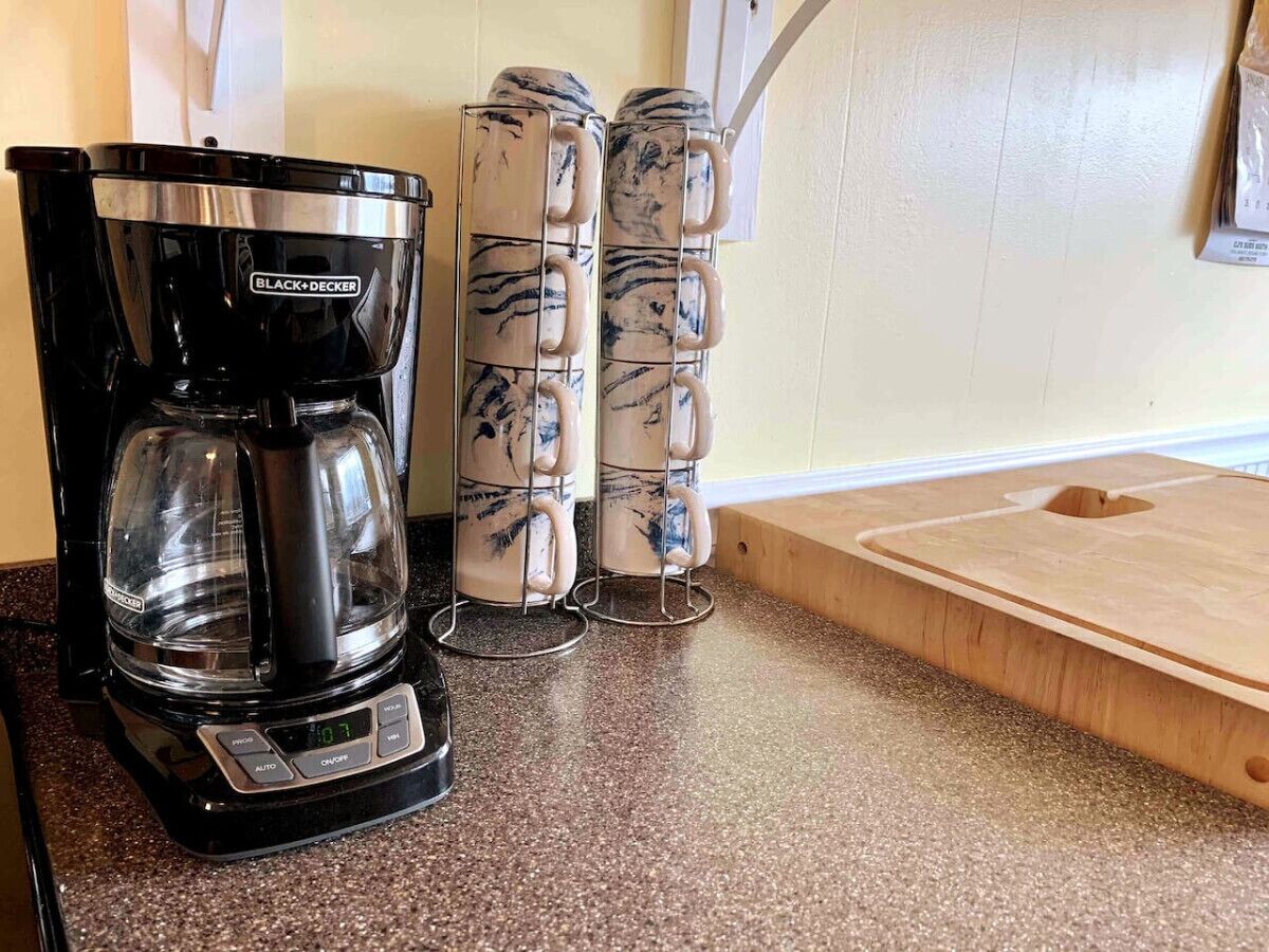 Une machine à café, une pile de tasses et une planche à découper en bois sur un plan de travail de cuisine.