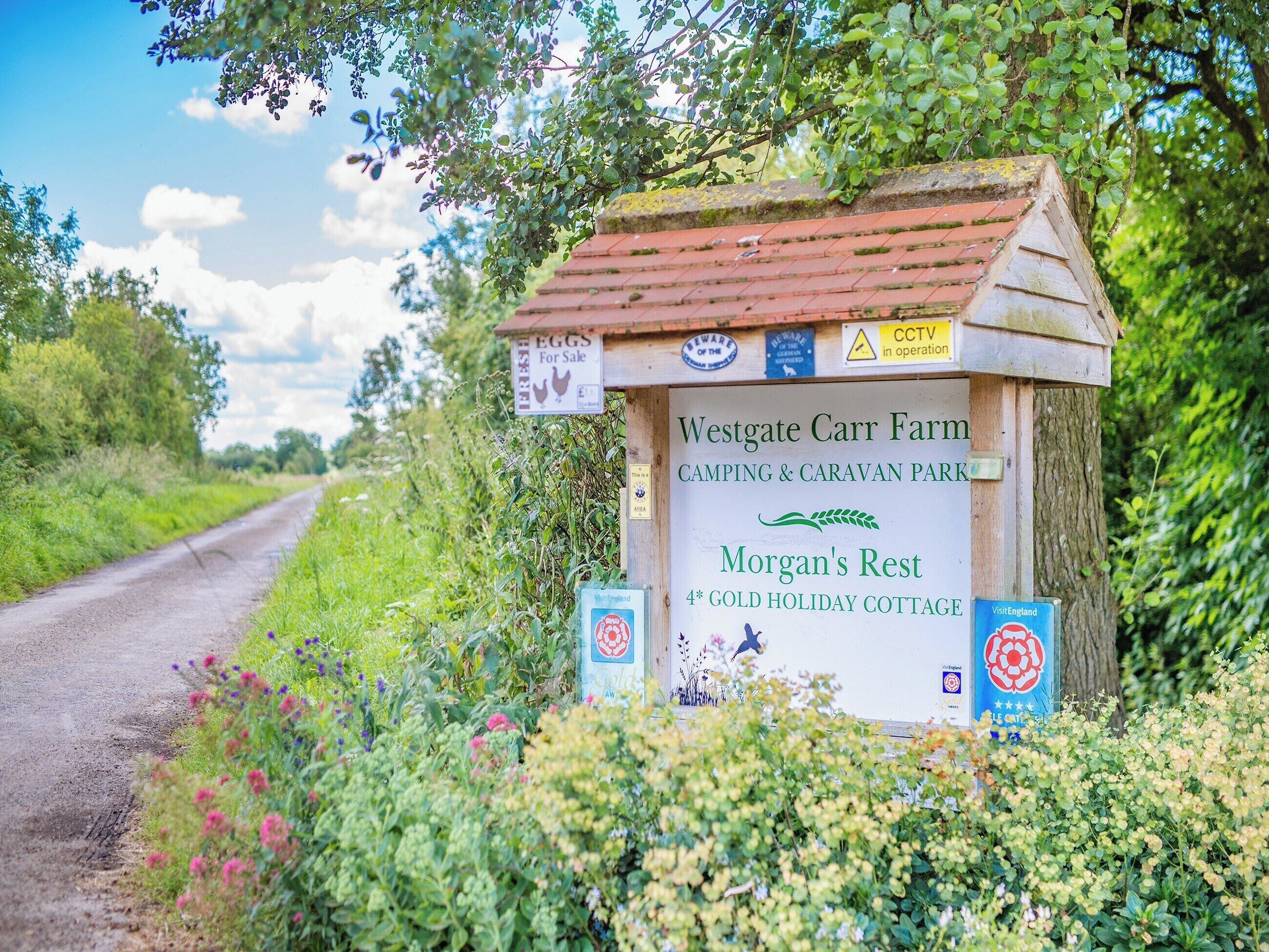 A rustic wooden sign for Westgate Carr Farm, indicating it is a camping and caravan park with a 4* gold holiday cottage named Morgan's Rest.