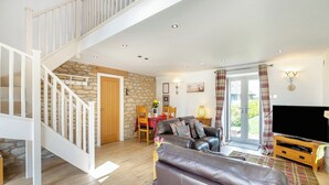 A spacious living room with a staircase, a leather sofa, a dining area, and a TV. - 1 bedroom accommodation in Pickering (Pickering)