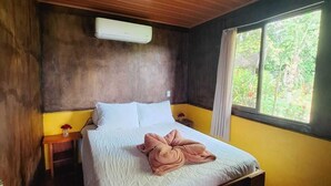 A wooden-paneled bedroom with a bed, bedside tables, and a window with a view of greenery. - Cabaña Refugio, located in the middle of nature. (La Fortuna)