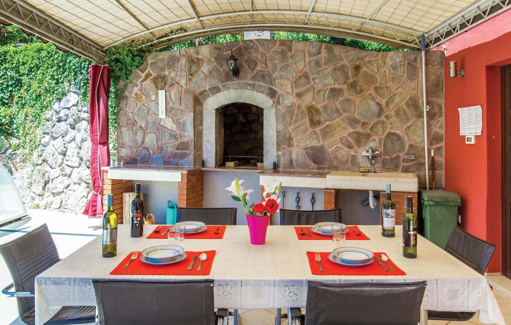 Uma área de refeições ao ar livre com parede de pedra e churrasqueira embutida, com uma mesa posta para dois e diversas garrafas.