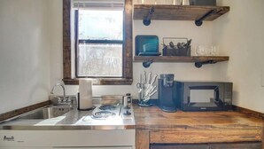A kitchen with a stove, sink, and microwave. There are wooden shelves above the counter holding dishes and utensils.