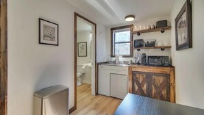 A compact kitchen with a wooden cabinet, a microwave, and a window above the sink.