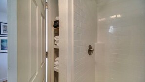Une salle de bain avec des murs carrelés de carreaux blancs, une porte de douche et un porte-serviettes avec des serviettes et une casquette noire.