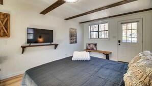 Une chambre à coucher avec un grand lit, un téléviseur fixé au mur, un banc et une porte avec des fenêtres.