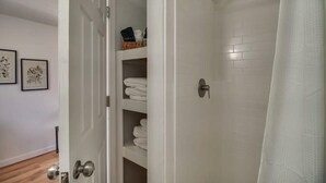 Une salle de bain avec une douche, une porte blanche et une étagère avec des serviettes.