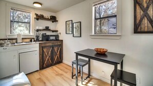 Une cuisine de taille réduite avec des meubles blancs, un plan de travail noir et une table à manger en bois.