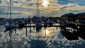 Un port de plaisance où sont amarrés de nombreux bateaux, une eau calme qui reflète le ciel et une structure en bois sur la droite.