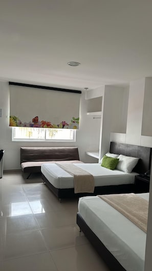 A modern bedroom with two beds, a window with a floral view, and a ceiling light. - HGO HOTEL  (Cali)