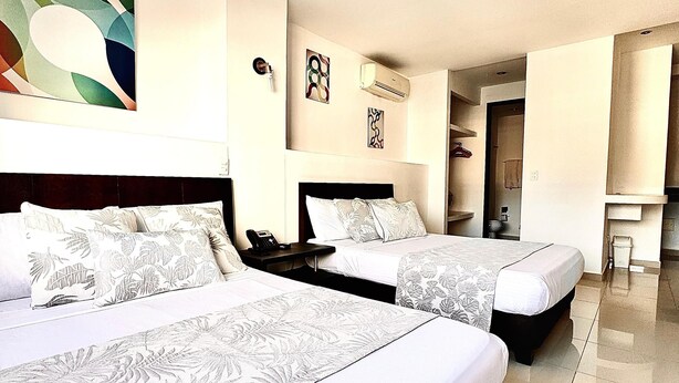 Quarto de hotel com duas camas, um quadro abstrato grande na parede e um banheiro visível através de uma porta aberta.