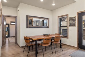 A dining area with a wooden table and four chairs, a large mirror on the wall, and a window with blinds. - Close to ski mountain, private hot tub! (Red Lodge)