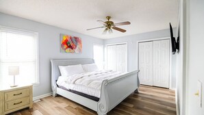 A bedroom with a bed, a ceiling fan, a window with blinds, and a door.