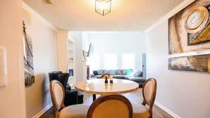 A dining area with a round table and four chairs, a black leather sofa, and a painting on the wall.
