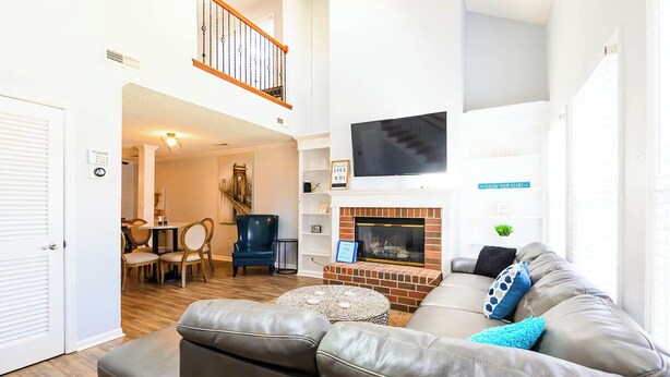 A spacious living room with a fireplace, leather sofa, and a dining area with chairs.