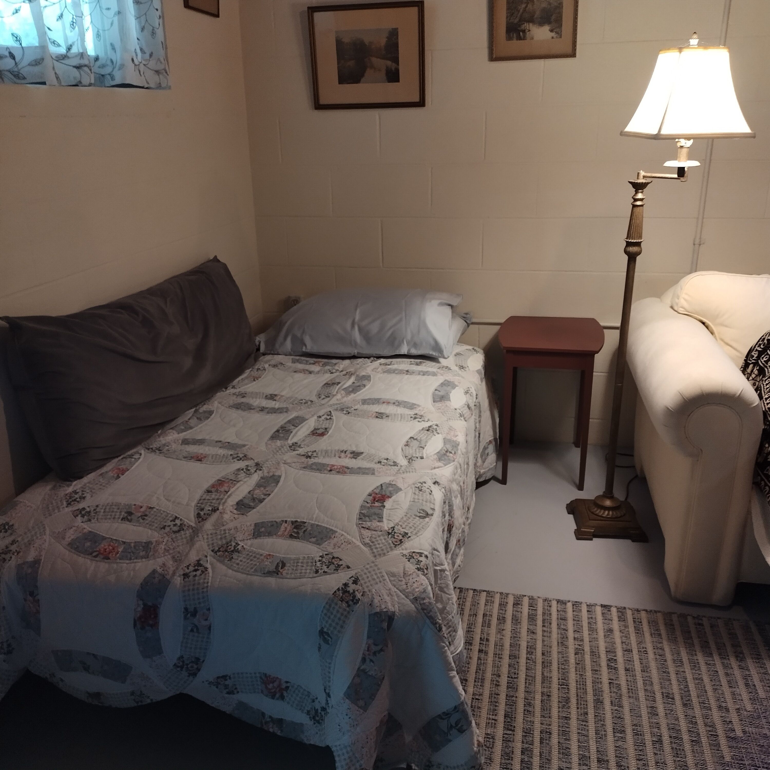 A small, cozy room with a single bed, a nightstand, a lamp, and a chair.