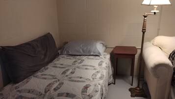 A small, cozy room with a single bed, a nightstand, a lamp, and a chair.