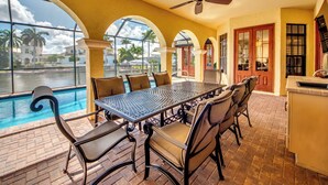 A dining area with a pool view, featuring a table and chairs, a ceiling fan, and a kitchen area with a sink and cabinets. - Heated Pool - Wide Gulf Access Canal - BBQ - Dock (Cape Coral)