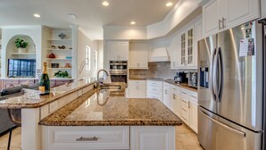 A modern kitchen with white cabinetry, a stainless steel refrigerator, granite countertops, and a built-in oven. - Heated Pool - Wide Gulf Access Canal - BBQ - Dock (Cape Coral)