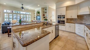 A spacious kitchen with granite countertops, white cabinetry, and a large island. - Heated Pool - Wide Gulf Access Canal - BBQ - Dock (Cape Coral)