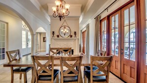 A spacious dining area with a large wooden table and chairs, a chandelier, and a fireplace. - Heated Pool - Wide Gulf Access Canal - BBQ - Dock (Cape Coral)