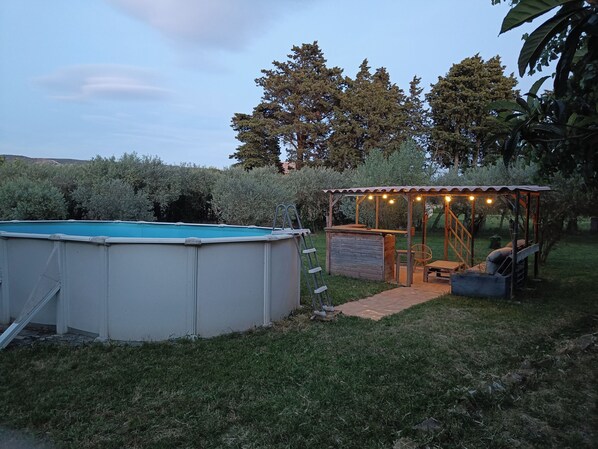 A backyard with a swimming pool, a wooden deck, and a covered seating area with string lights.