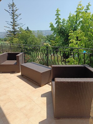 A balcony with wicker furniture and a view of greenery and mountains.