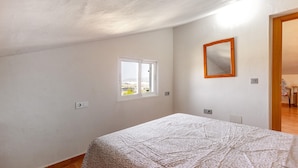 Ein Schlafzimmer mit Bett, Fenster, Spiegel und Tür.