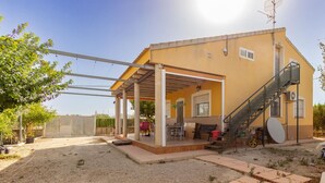 Ein zweistöckiges Gebäude mit überdachter Terrasse, Außenmöbeln und einer Treppe, die zu der oberen Etage führt.