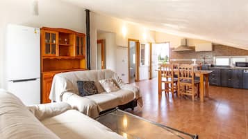 A spacious living area with a sofa, a glass coffee table, and a dining table with chairs. There is a kitchen area with a stove, microwave, and cabinets.