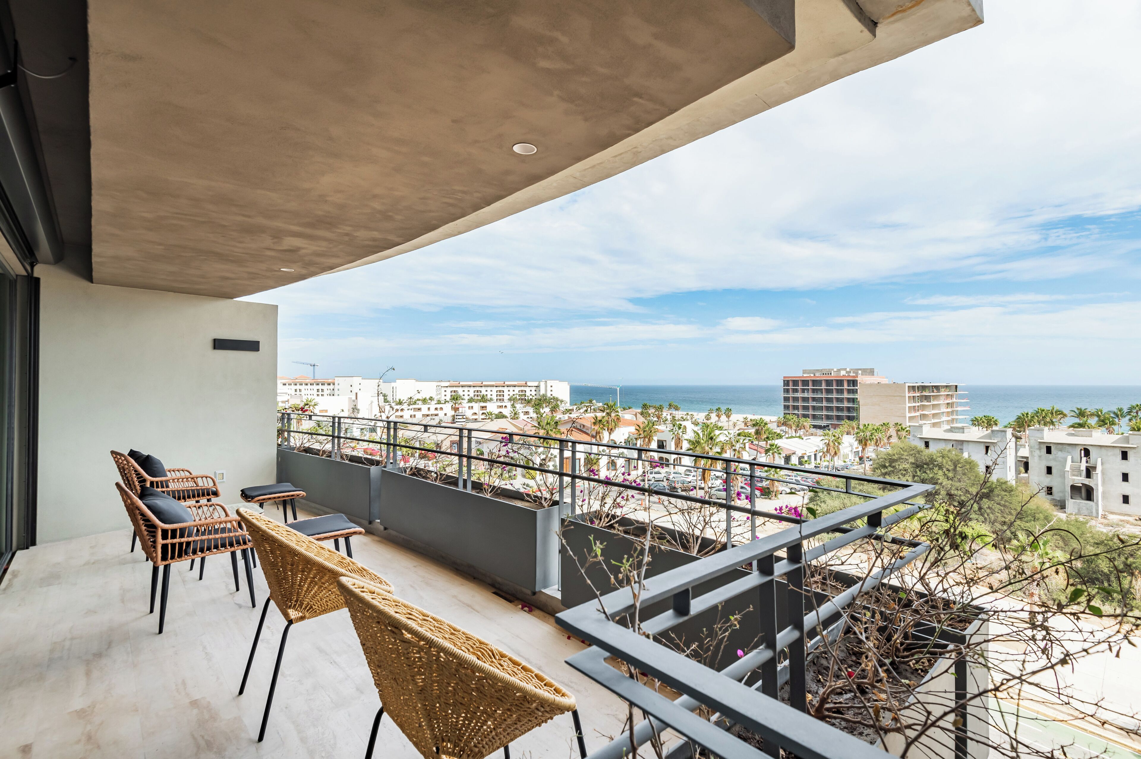 Uma varanda com móveis de vime, vista para o mar e edifícios ao fundo.