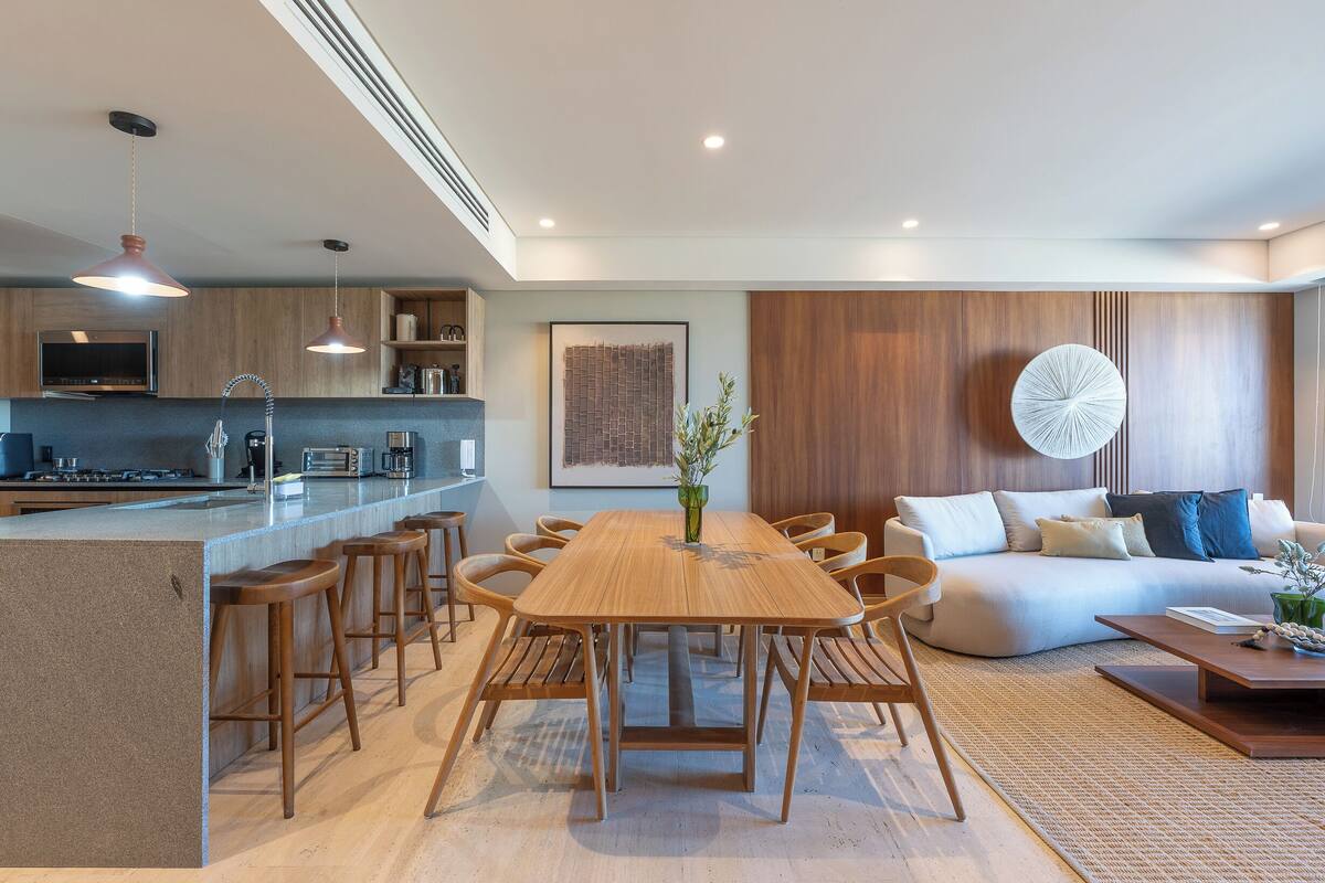 A modern kitchen with a central island, wooden bar stools, and a dining table with chairs.