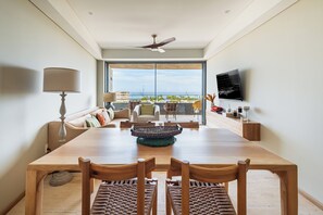 Een eetruimte met een houten tafel en stoelen, een plafondventilator en uitzicht op de oceaan door grote ramen.