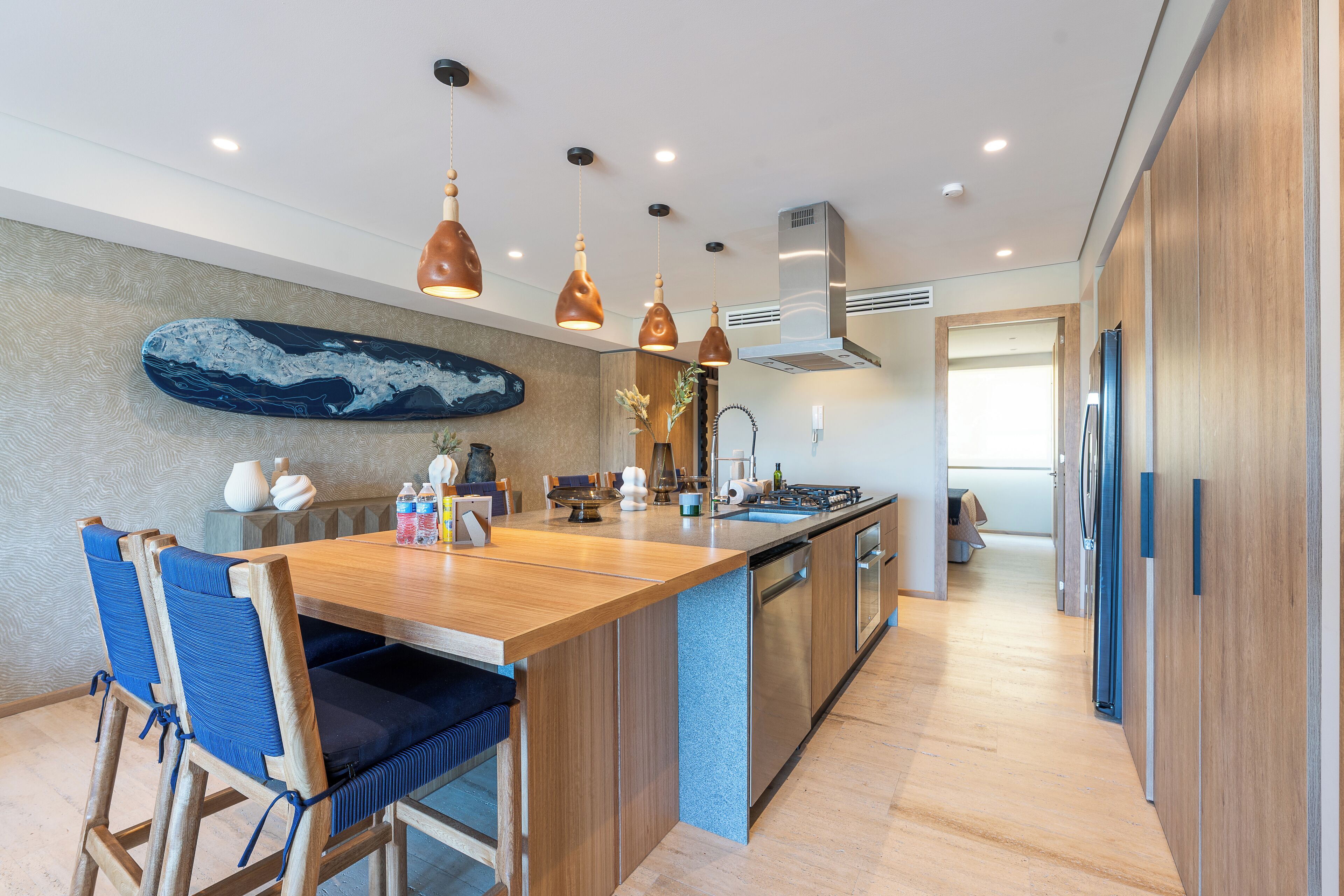 A modern kitchen with a wooden island, pendant lighting, and a large decorative piece on the wall.